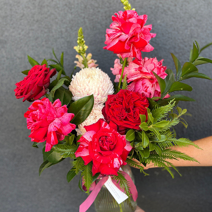 Bouquet of red and pink flowers with green leaves held against a gray background