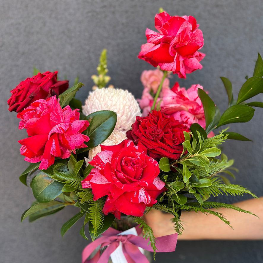 Bouquet of red and pink flowers held by a person against a gray background